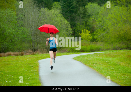 Gemischte Rassen Läufer training auf remote-Straße mit Regenschirm Stockfoto