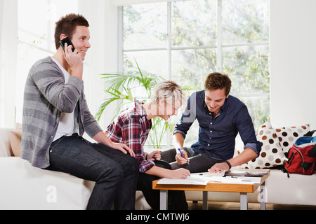Junger Mann am Telefon während Freunde studieren im Hintergrund Stockfoto