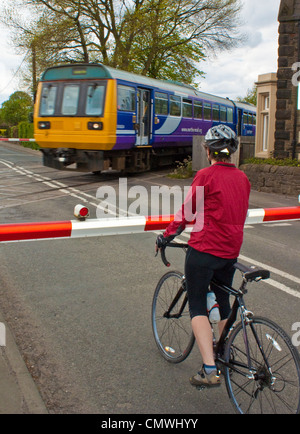 Frau Radfahrer warten auf Zug am Bahnübergang in der Nähe von Burscough in West Lancashire Stockfoto