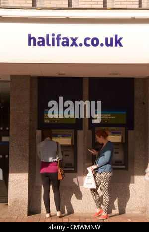 Junge Frau mit Cashpoint Maschine, während ein anderes ihr Handy, High Street, Gosport, Hampshire, UK überprüft. Stockfoto