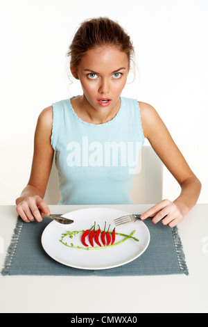 Porträt von hübsches junges Mädchen mit Gabel und Messer in Händen und Platte mit rote scharfe Chilischoten vor Stockfoto