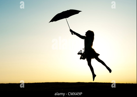 Junges Mädchen springen mit einem Sonnenschirm und Teddybär bei Sonnenuntergang. Silhouette. UK Stockfoto