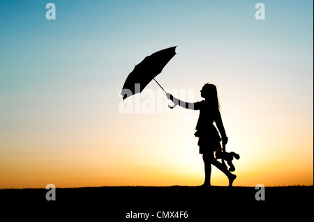 Junge Mädchen zu Fuß mit einem Regenschirm und Teddybär bei Sonnenuntergang. Silhouette.UK Stockfoto