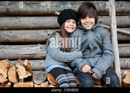 Deutschland, Huglfing, Mädchen und junge sitzt auf Stapel Brennholz, Lächeln, Porträt Stockfoto