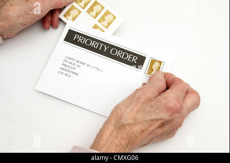 Ältere Frau setzen eine 1. erstklassige Stempel auf einem Umschlag bereit für Entsendung (Preiserhöhungen 30. April 2012 Stockfoto