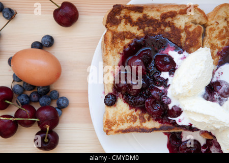 French Toast mit Grütze vermischt und Double Schlagsahne fotografiert bei Tageslicht auf einem weißen Teller mit Ei & Beeren Stockfoto