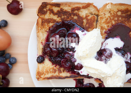 French Toast mit Grütze vermischt und Double Schlagsahne fotografiert bei Tageslicht auf einem weißen Teller mit Ei & Beeren Stockfoto