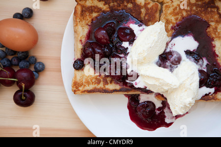 French Toast mit Grütze vermischt und Double Schlagsahne fotografiert bei Tageslicht auf einem weißen Teller mit Ei & Beeren Stockfoto