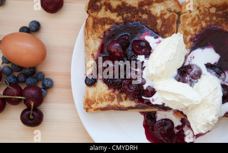 French Toast mit Grütze vermischt und Double Schlagsahne fotografiert bei Tageslicht auf einem weißen Teller mit Ei & Beeren Stockfoto