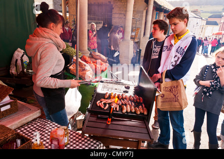 Junge Frau Standinhaber Kochen Würstchen am Samstag Bauernmarkt in Stroud, Gloucestershire, UK Stockfoto