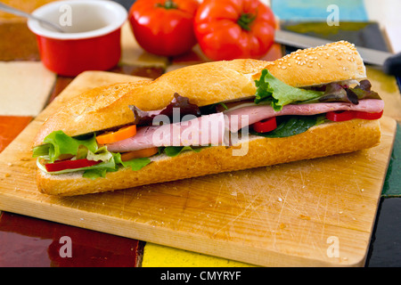 Schinken-Salat-Sandwich-Baguette auf ein Schneidbrett aus Holz. Tomaten im Hintergrund Stockfoto