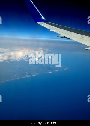 aus einem Flugzeug-Fenster zeigt die Flugzeugflügel mit blauem Meer und Land unten anzeigen Stockfoto