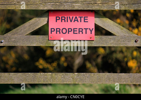 Eine kühne rote Schild mit der Aufschrift Privateigentum auf einem vergitterten Tor in der Landschaft Stockfoto