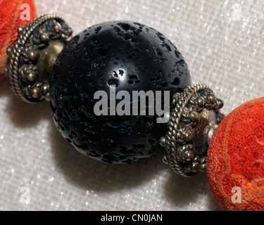 Ein schwarzer Lava Stein zwischen zwei Korallen Perlen an einer Hand gearbeitete Halskette auf einer Kunstmesse aufgereiht. Stockfoto