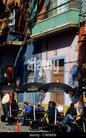 Gäste sitzen in einem Straßencafé unter schwarzen Sonnenschirmen neben farbenfrohen historischen Gebäuden in La Boca, Buenos Aires, Argentinien. Stockfoto