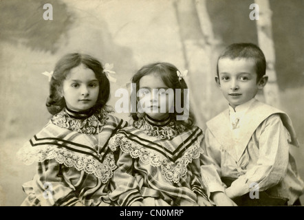 1908er Jahre altes sepiafarbenes Bild mit zwei kleinen Mädchen und einem kleinen Jungen, Schwestern, ernsthaftem Porträt, 3 Kinderporträts Stockfoto