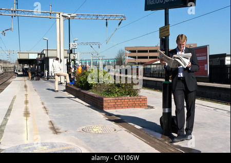 Mann liest Zeitung warten auf einen Zug am Bahnhof Watford Junction Stockfoto