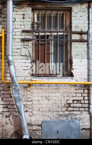 Vergitterte Fenster, Kabel und Wasserpfeife auf heruntergekommenen Ziegelwand Stockfoto