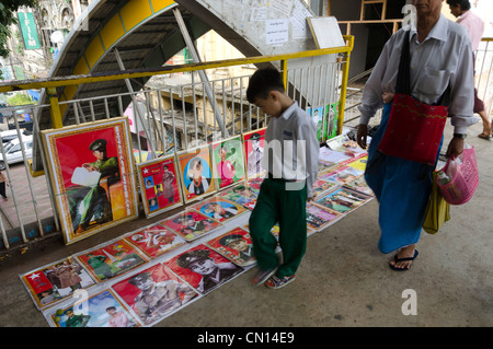 Kind beobachten Poster von The Lady und general Aung San für Verkauf in den Straßen von Yangon. Myanmar. Stockfoto