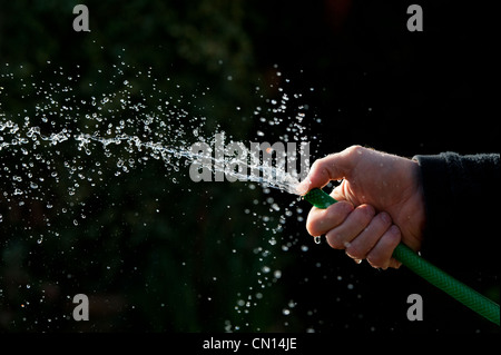 Hand mit Gartenschlauch vor einem dunklen Hintergrund Sprühwasser Stockfoto