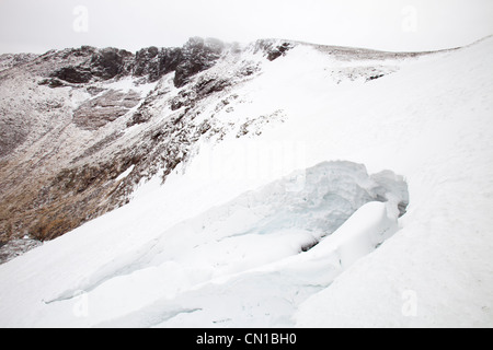 Ein Loch verursacht durch eine Schneewehe über den Rand eines Baches in Coire einstürzenden eine Lochain in Cairngorm Mountains, Schottland, Großbritannien. Stockfoto