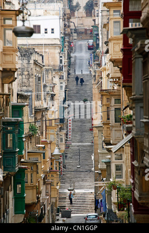 Straßenszene mit überdachten Holzbalkonen und lange Flüge der Treppe auf einem Hügel in Valletta, Malta Stockfoto