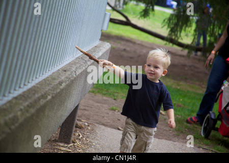 Blonde junge läuft durch Zaun mit Stick Stockfoto