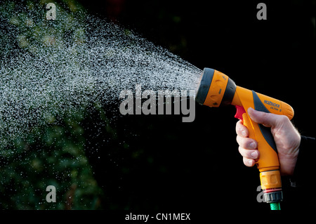 Gärtner Hand sprühen Wasser mit Gartenschlauch gegen einen dunklen Hintergrund. Großbritannien Stockfoto