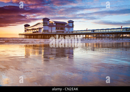 Sonnenuntergang über dem Grand Pier bei Weston-Super-Mare, Somerset, England, UK spiegelt sich in dem nassen Sand des Strandes bei Flut. Stockfoto