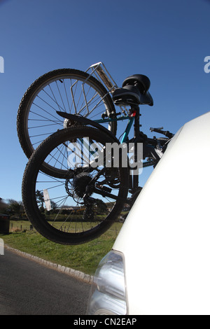 Zwei Fahrräder montiert auf der Rückseite von einem silbernen Auto fahren durch eine ländliche Umgebung. Stockfoto