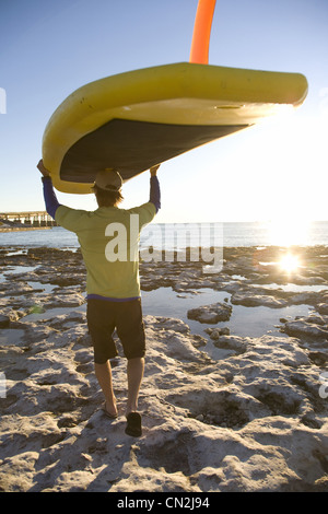 Mann trägt Paddleboard am Strand, Florida Keys, USA Stockfoto