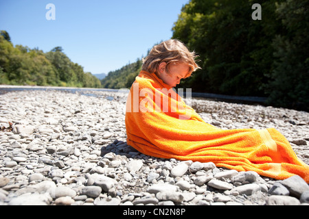 Junge gewickelt Handtuch sitzen auf Felsen Stockfoto