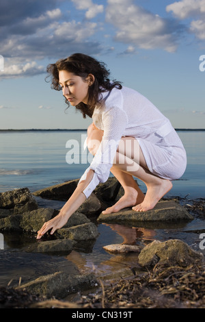 Frau in weißem Kleid hocken auf Felsen auf dem Seeweg Stockfoto