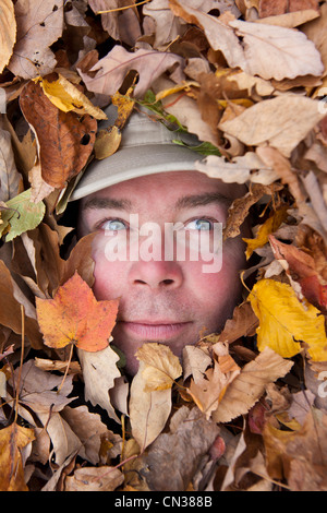 Das Gesicht des Mannes spähte durch Herbst Blätter Stockfoto