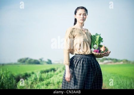 Junge Frau im Feld Betrieb Korb mit einheimische Gemüse Stockfoto