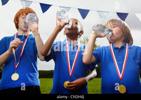 Schule Jungs mit Medaillen Trinkwasser nach Sport-event Stockfoto