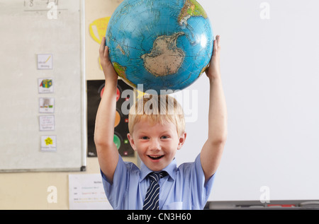 Schuljunge Globus über seinen Kopf in einem Klassenzimmer zu halten Stockfoto