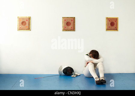 Weibliche Fechter mit Kopf in Händen gegen die Wand sitzen Stockfoto