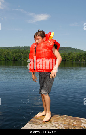 Kleiner Junge stehend auf einem Dock tragen mehrere Schwimmwesten Stockfoto