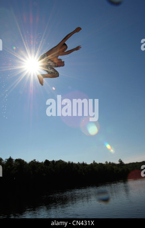 Young Boy springen weg von einem Dock mit Sonnenlicht hinter ihm, Lac des Neiges, Quebec Stockfoto