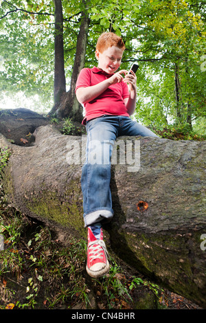 Junge sitzt auf einem Baumstamm mit dem Handy telefonieren Stockfoto