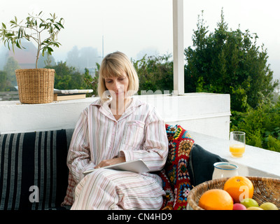 Reife Frau trägt Pyjama mit Laptop auf Balkon Stockfoto