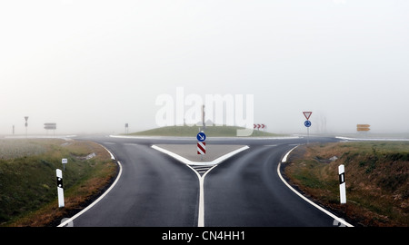 Kreisverkehr und Straße mit den Zeichen im Nebel Stockfoto