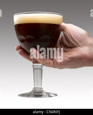 Mannes Hand hält ein Trappist Bier Glas auf Farbverlauf grauen Hintergrund (Clipping-Pfad) Stockfoto