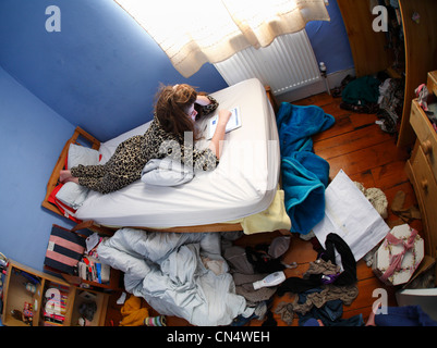 Teenager-Mädchen mit einem Ipad auf ihrem Bett in einem chaotischen Schlafzimmer. Stockfoto
