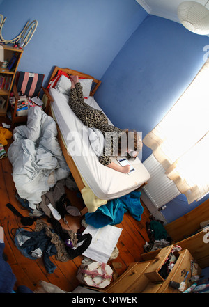 Teenager-Mädchen mit einem Ipad auf ihrem Bett in einem chaotischen Schlafzimmer. Stockfoto