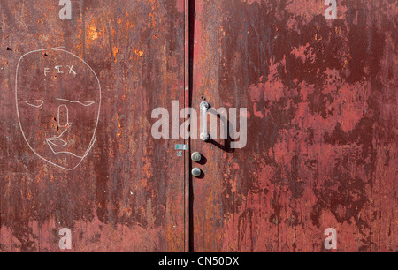 Rote Tür und Griff mit abblätternde Farbe und Gesicht gezeichnet in weißer Stift mit dem Wort fix Stockfoto