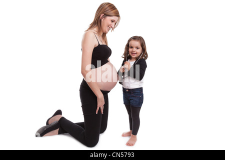 Kleines Mädchen untersuchen ihre schwangere Mutter mit einem Stethoskop, isoliert auf weißem Hintergrund Stockfoto