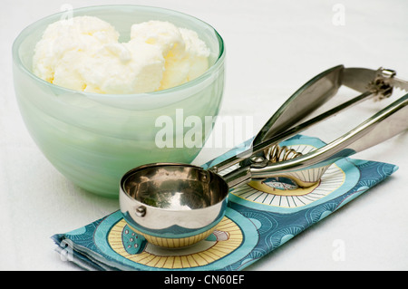 Vanille-Eis in einer Milchglas-Schüssel mit einem Eisportionierer. Stockfoto