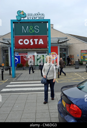 Frau außerhalb eine MOTO Autobahnraststätte auf der M6 in Stafford mit eine M & S Shop und Costa Coffee shop Stockfoto